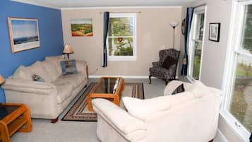 A living room with a beige sofa, a patterned armchair, a glass coffee table, and a rug.