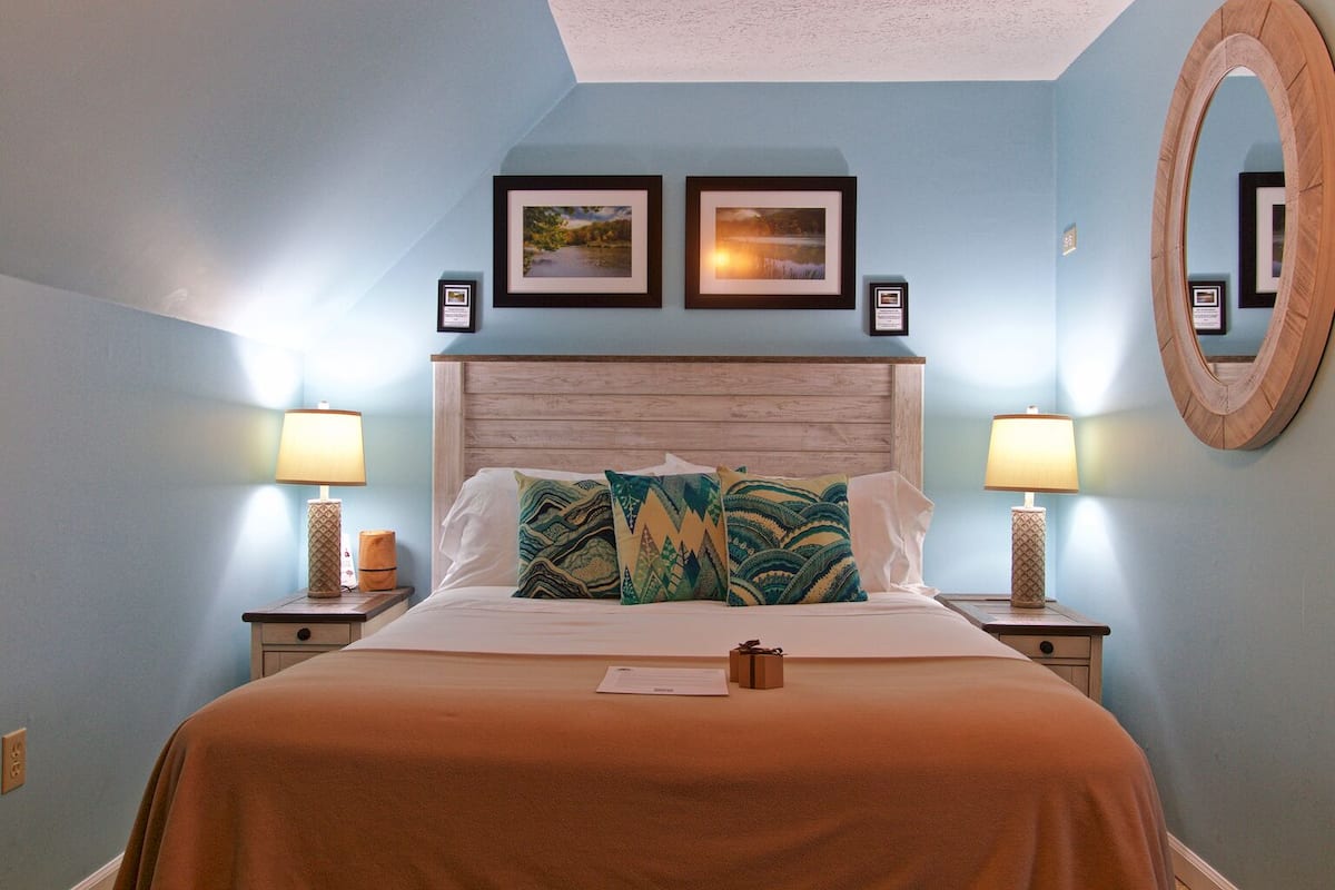 A bedroom with a bed, two nightstands, a mirror, and two framed pictures on the wall.