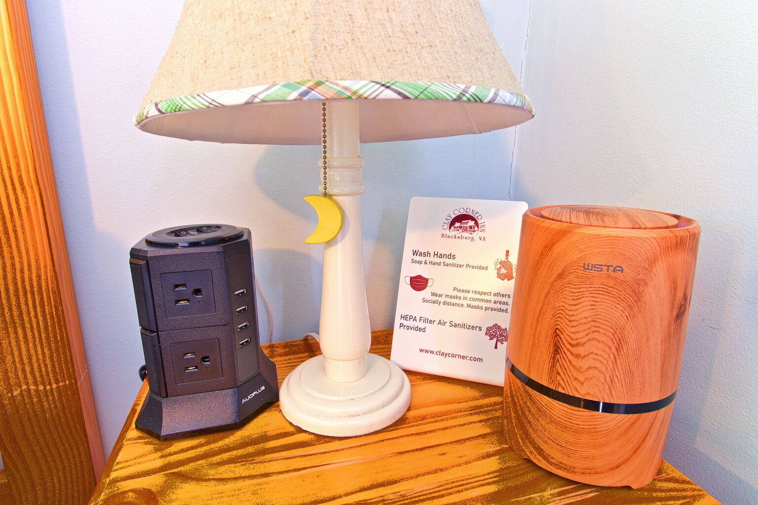 A lamp with a moon-shaped base, a black device with multiple ports, and an orange cylindrical object on a wooden surface.