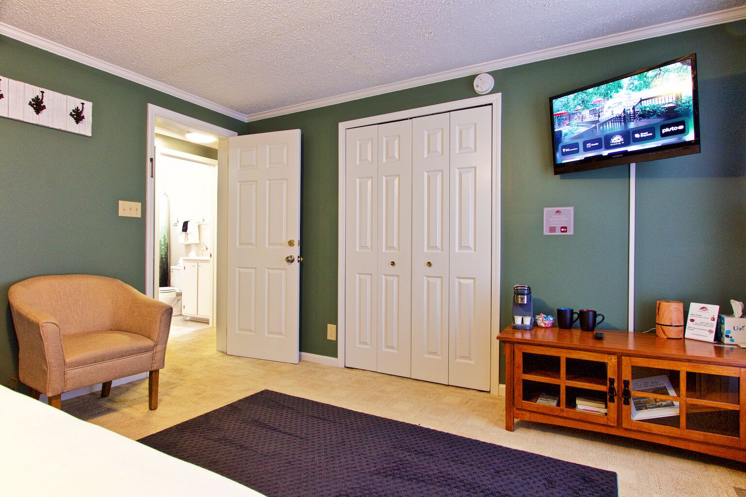 A room with a beige armchair, a wooden coffee table, a flat-screen TV, and a set of white doors.
