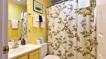 A bathroom with yellow walls, a white sink, and a shower curtain with a bird and flower pattern.
