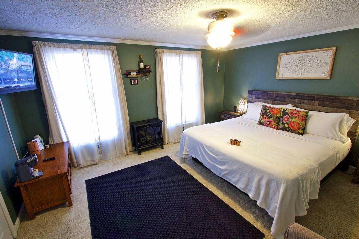 A bedroom with a bed, a nightstand, a dresser, a television, and a window with curtains.