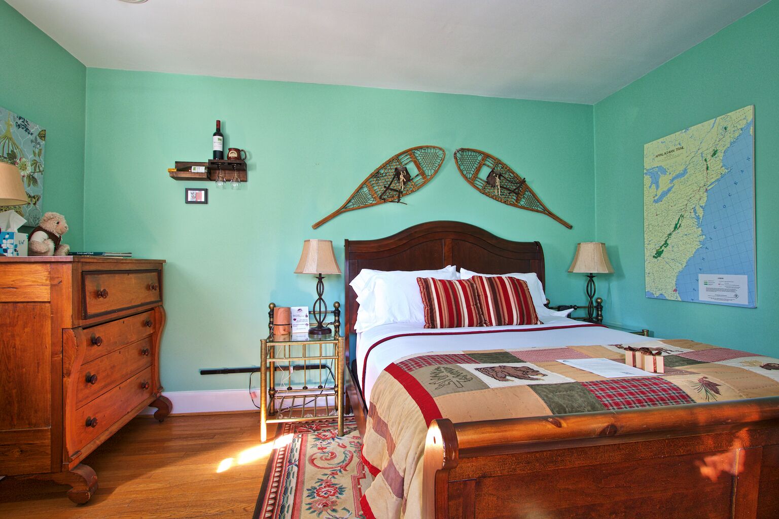 A bedroom with a wooden bed, a wooden dresser, a small table with a lamp, and a map on the wall.