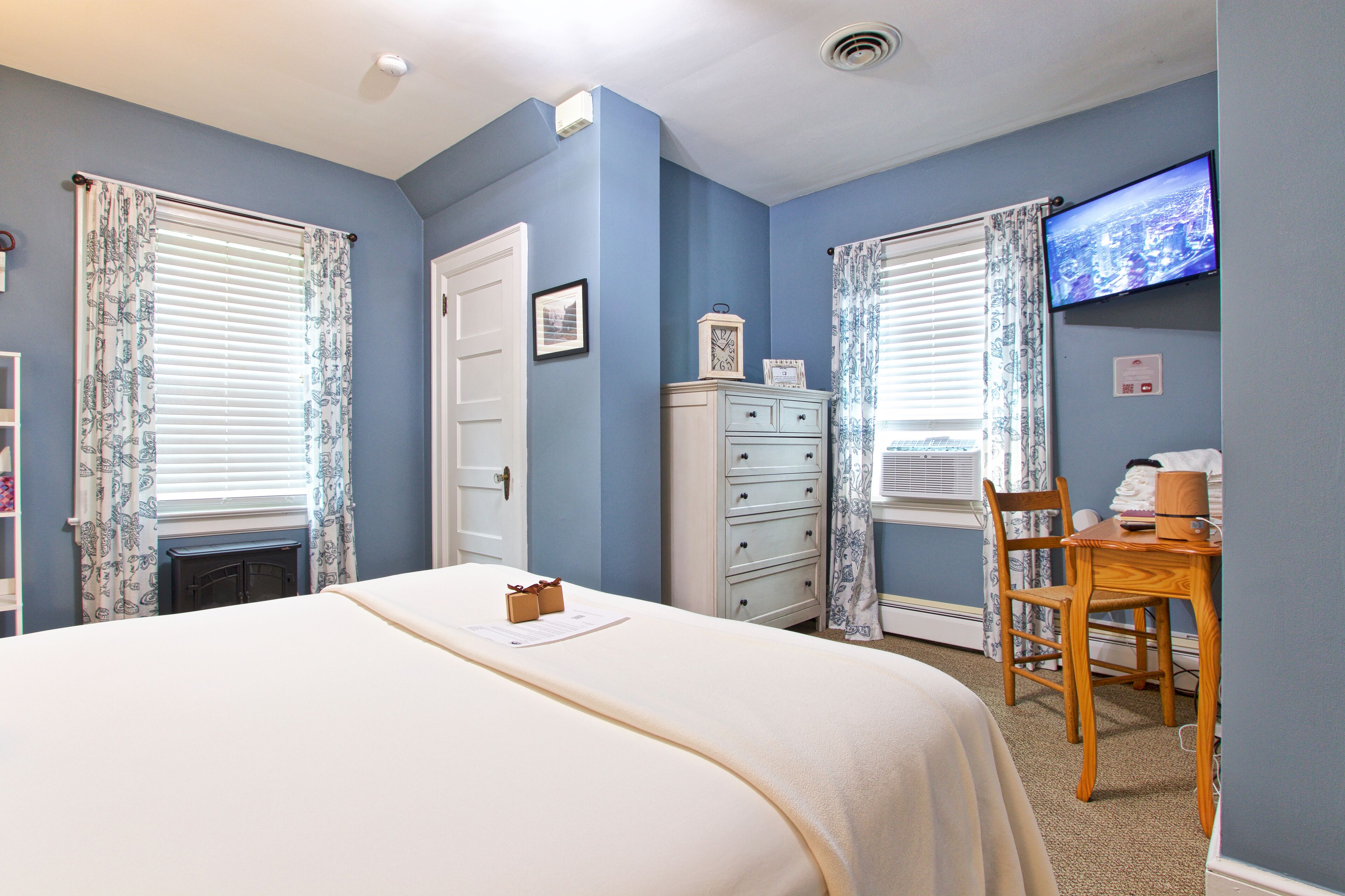 A bedroom with a bed, a dresser, a chair, a television, and a window with curtains.