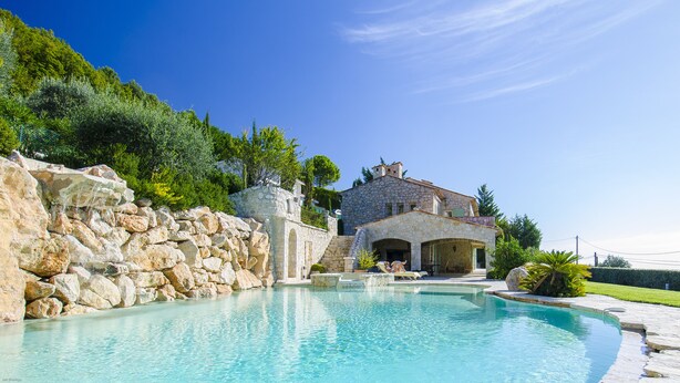 Una casa in pietra con piscina, un muro di pietra e un prato curato.