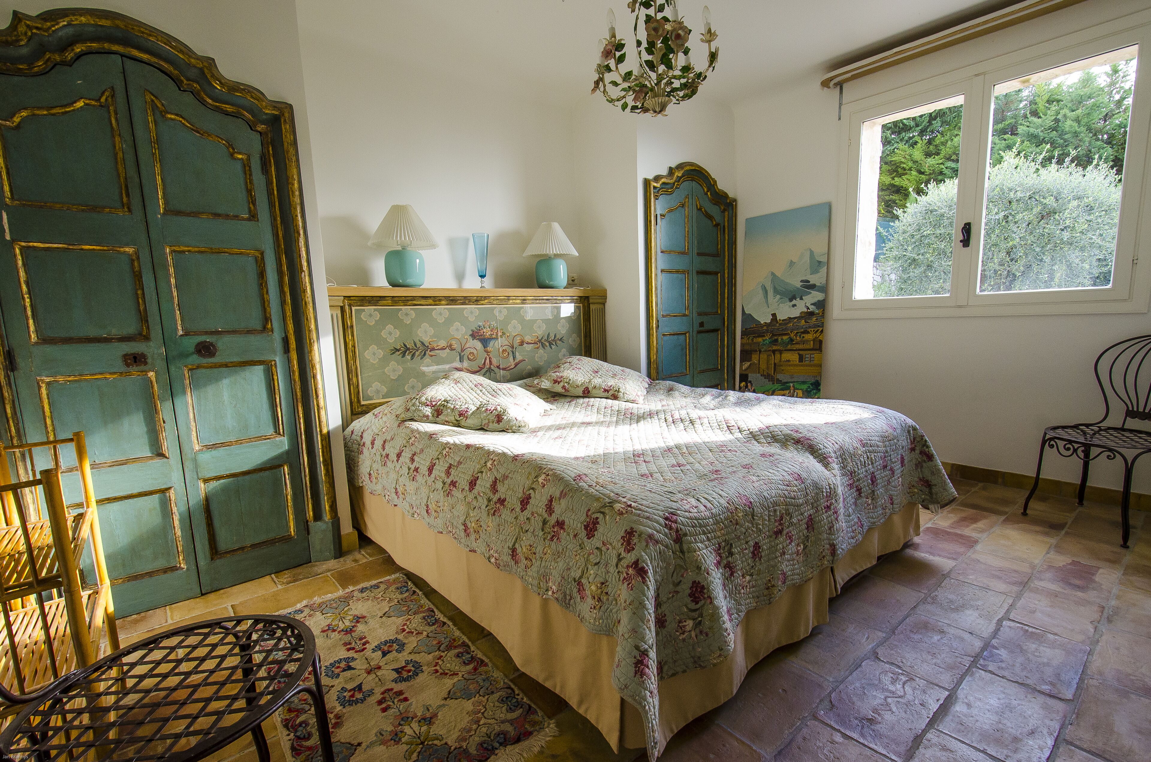 A bedroom with a large bed, a dresser, a chair, and a window with a view of trees.