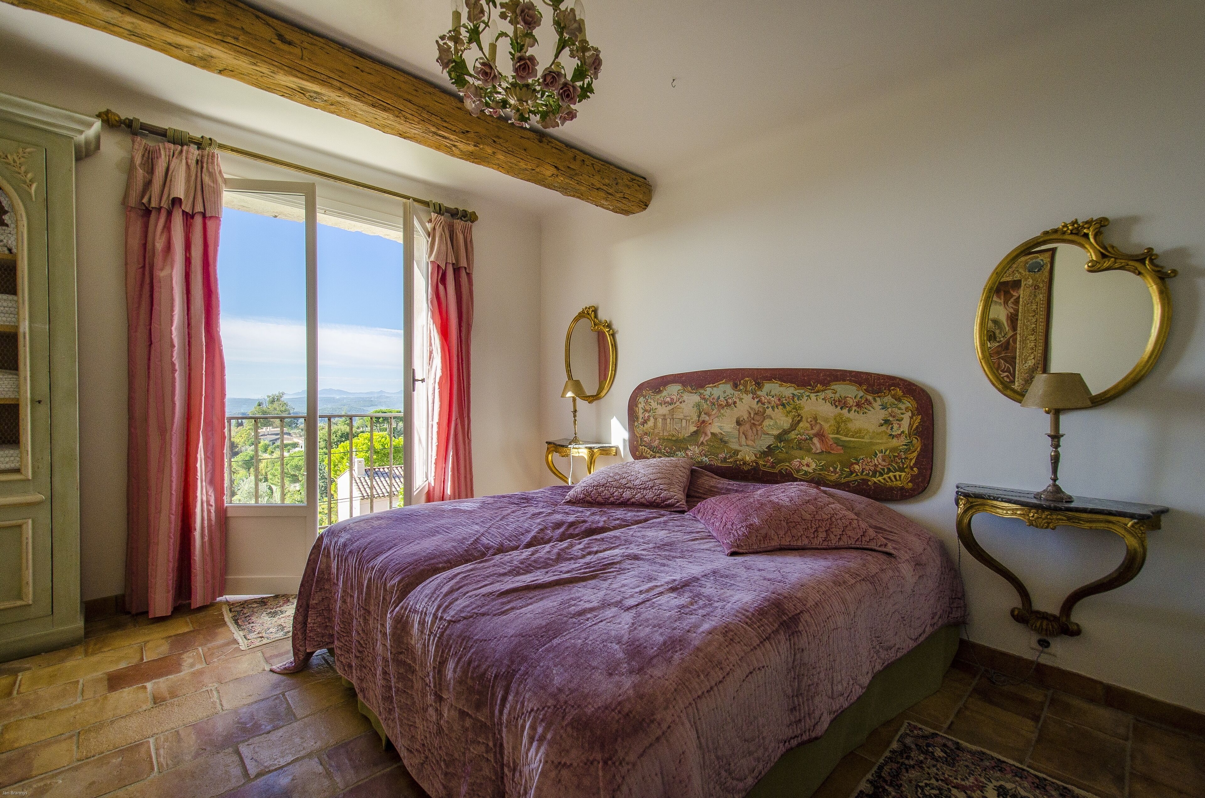 A bedroom with a large bed, a balcony view, a chandelier, and ornate furniture.