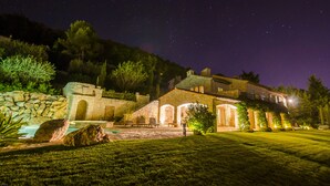 Una villa in pietra con piscina, area salotto esterna e giardino illuminato di notte.