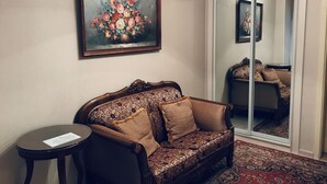 Ein Zimmer mit einer gemusterten Couch, einem kleinen Tisch, einem gerahmten Blumenbild und einer Schiebetür mit Spiegel.