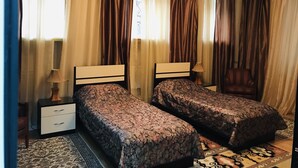 Ein Schlafzimmer mit zwei Einzelbetten, einem Nachttisch mit Lampe, einem Sessel und einem gemusterten Teppich.