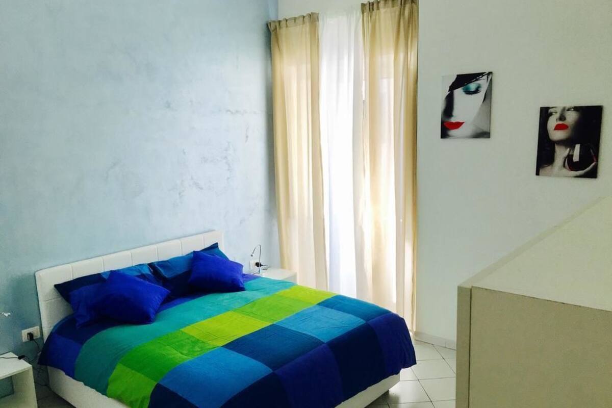Un dormitorio con cama, cortinas y dos cuadros en la pared.