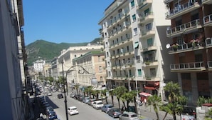 A street lined with multi-story buildings, parked cars, and palm trees.