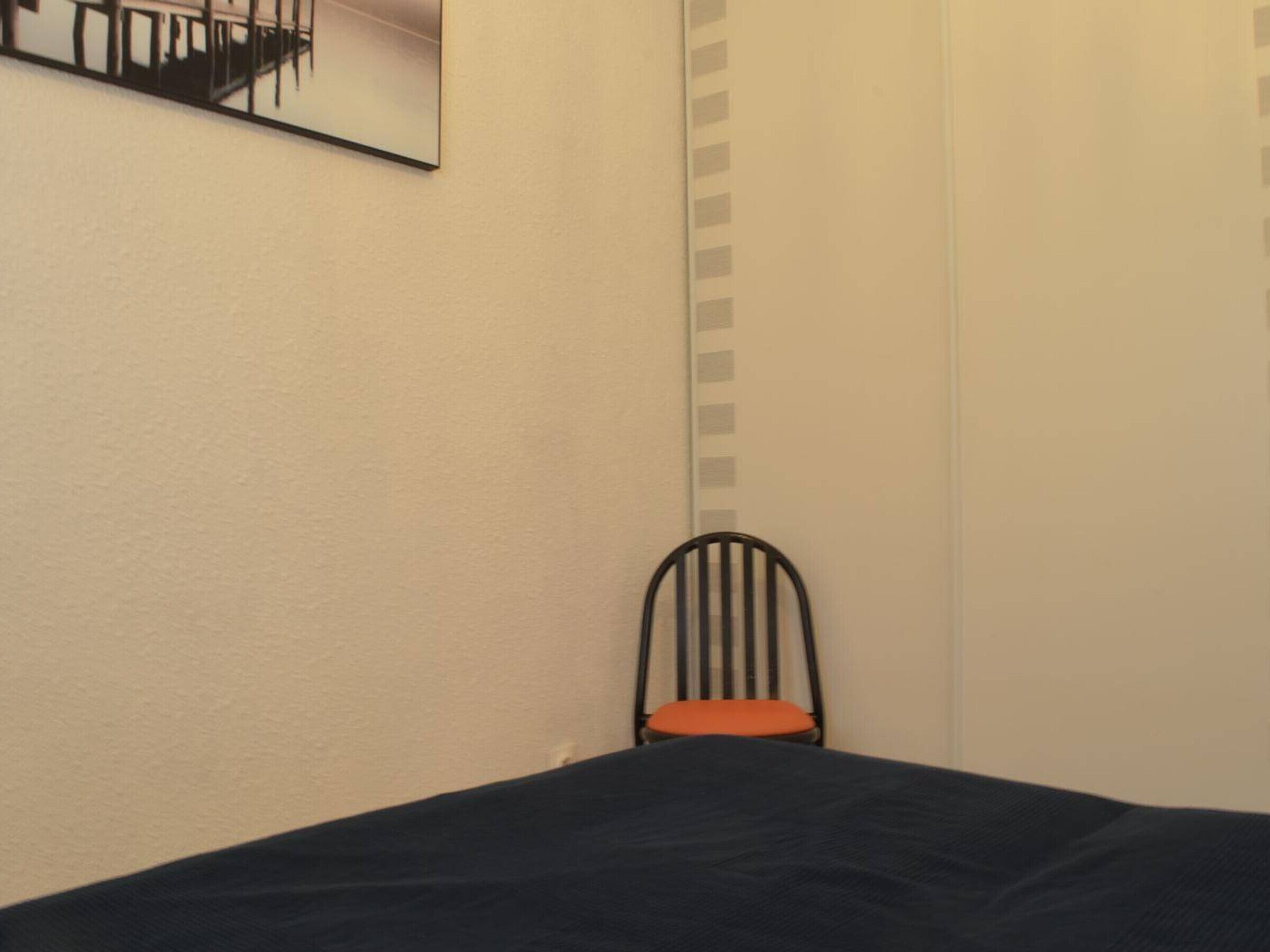 A room with a bed, a chair, and a wall-mounted picture.