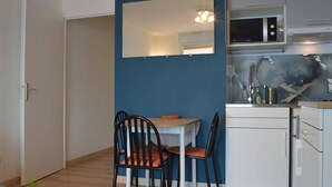 Ett kompakt kök med mikrovågsugn, diskho och skåp. Det finns ett matbord med stolar och en spegel ovanför.