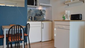 Ett litet, praktiskt kök med mikrovågsugn, spishäll och kaffebryggare. Det finns en liten matplats med ett bord och två stolar.