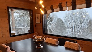 A wooden cabin interior with a large table, two chairs, a decorative bowl, and a window with a snowy view. - Large chalet 12 people (Les Angles)