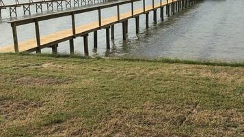 Une jetée en bois s’étendant dans une étendue d’eau calme, avec une zone herbeuse au premier plan.