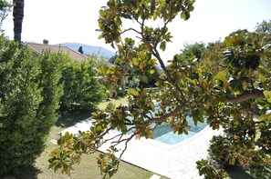 Un jardin aménagé avec une piscine, des haies soigneusement taillées et une vue dégagée sur une montagne en arrière-plan.