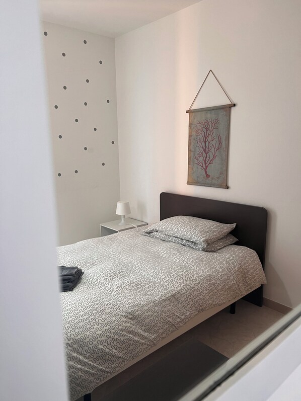 A bedroom with a bed, a nightstand, a wall-mounted artwork, and a patterned bedspread.