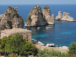 A coastal view with rocky formations, clear blue sea, and a building with a tiled roof.
