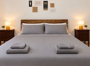 A neatly made bed with two pillows and two folded towels, flanked by two bedside tables with lamps and a small plant.