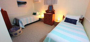 Ein Schlafzimmer mit zwei Einzelbetten, einem Schminktisch, einem Nachttisch mit Lampe und einer Wand-Klimaanlage.