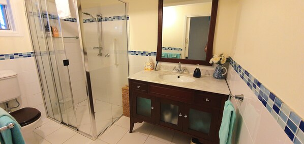 A bathroom with a glass-enclosed shower, a sink with a mirror, and a vase with flowers.