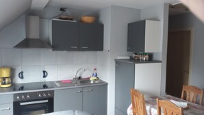 A compact kitchen with grey cabinets, a sink, a coffee maker, and a dining area with a table and chairs. - Cozy large vacation apartment, pet friendly, ideal f. Children, (Moorweg)