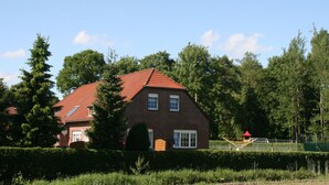 A brick house with a red roof, surrounded by greenery and trees. - Cozy large vacation apartment, pet friendly, ideal f. Children, (Moorweg)