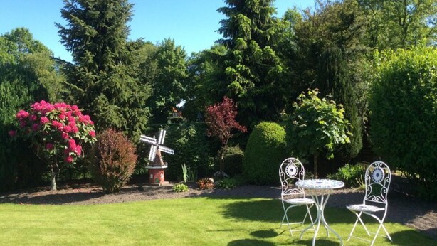 A garden with a windmill, two white metal chairs, and a table. - Cozy large vacation apartment, pet friendly, ideal f. Children, (Moorweg)