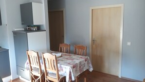 A dining area with a table covered by a floral tablecloth, surrounded by wooden chairs. There is a cabinet above the table and a door to the right. - Cozy large vacation apartment, pet friendly, ideal f. Children, (Moorweg)