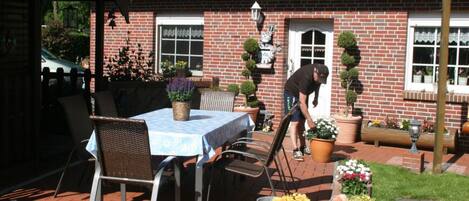 A patio area with a table and chairs, a brick building with a red-tiled roof, and potted plants.