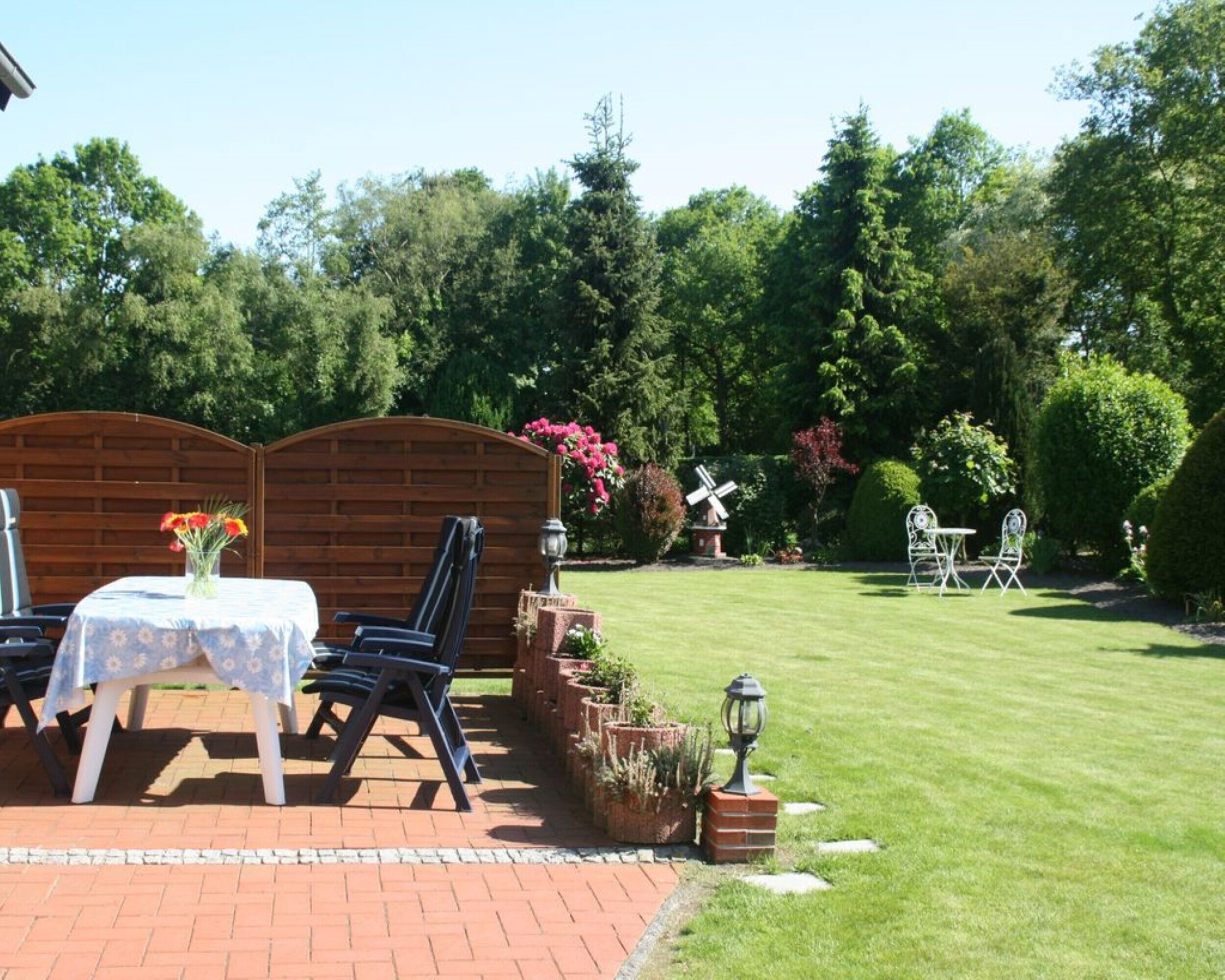 Une terrasse avec une table et des chaises, un chemin en briques et une pelouse bien entretenue.