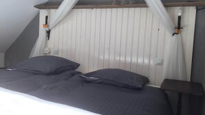 Une chambre avec un plafond en pente, un lit avec une literie sombre, une table de chevet et une lampe fixée au mur.