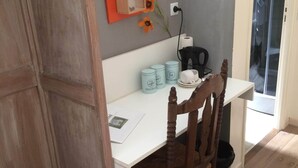Une pièce avec un cadre en bois, comprenant un bureau blanc, une chaise et une petite table sur laquelle est posé un vase de fleurs. Sur le bureau, on trouve trois récipients bleu clair, un sac noir et une tasse blanche.