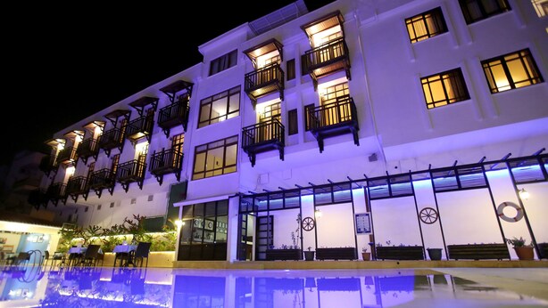 Un hotel de varios pisos con balcones, piscina y mobiliario de exterior.