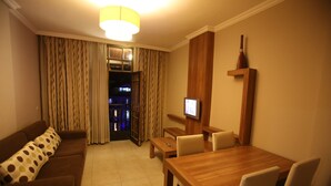 Una habitación de hotel con un sofá marrón, una mesa de comedor de madera y un televisor instalado en la pared.