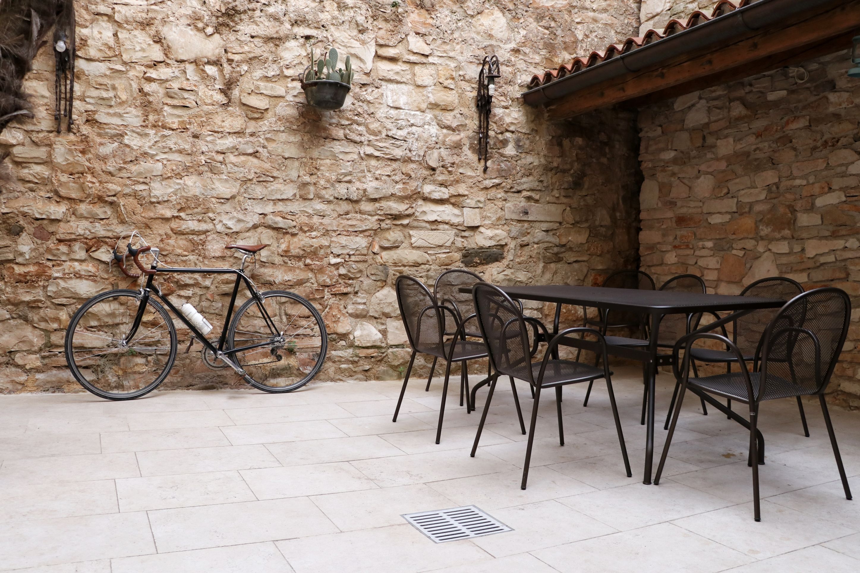 Een stenen muur met een fiets, een tafel met stoelen en een metalen hekwerk.