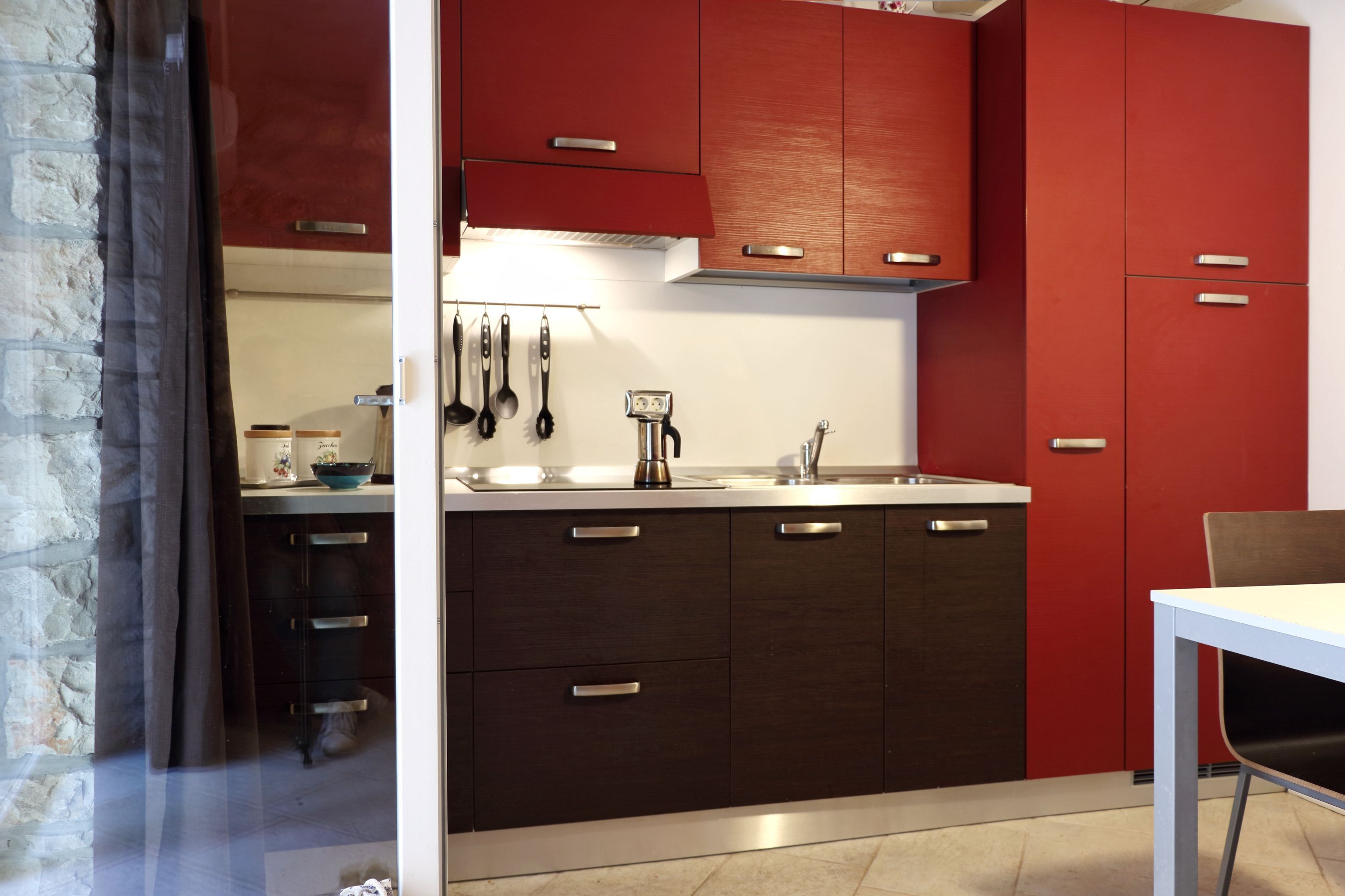 Une cuisine compacte avec des meubles de couleur sombre, un plan de travail blanc et un petit coin repas comprenant une table et une chaise.