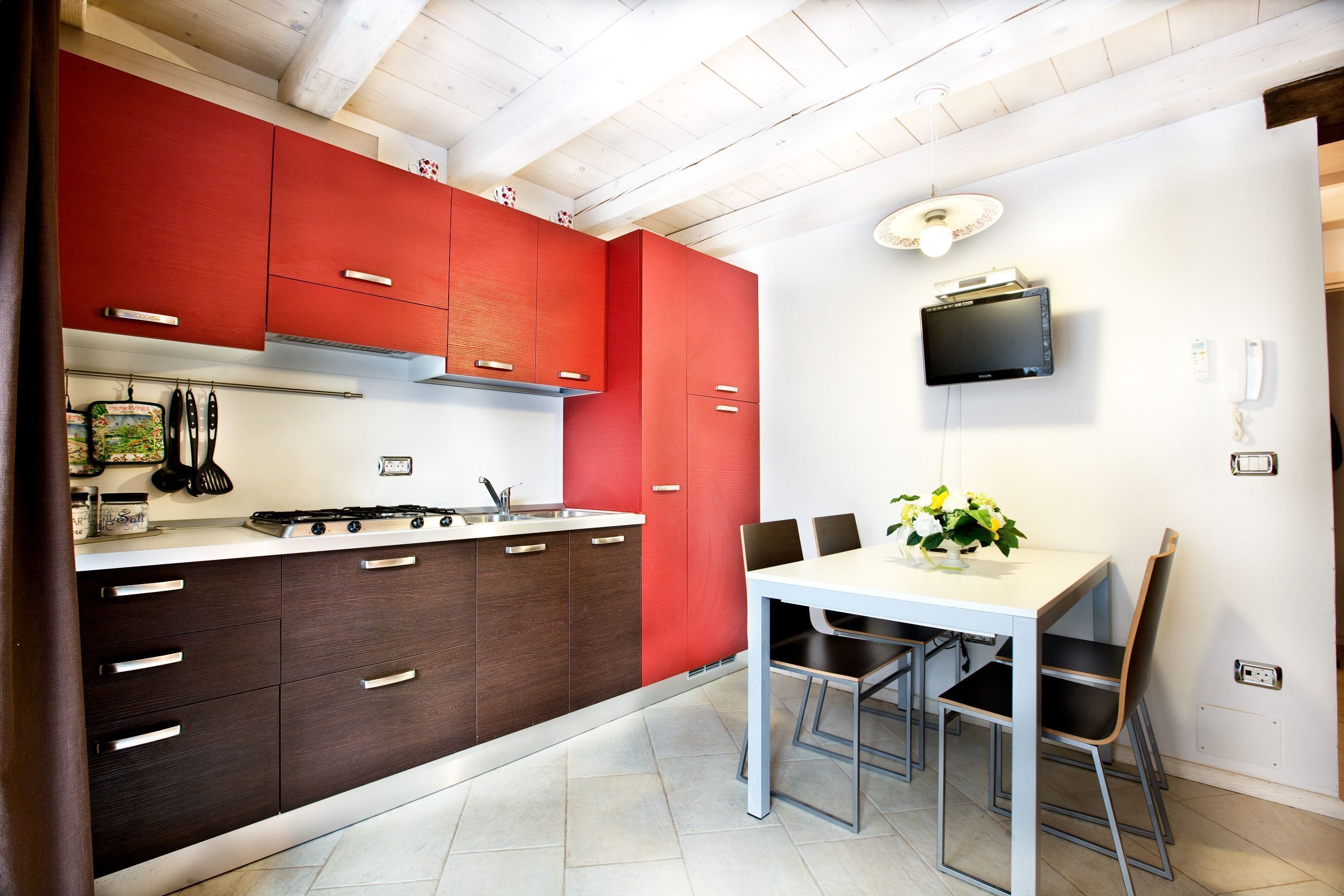 A modern kitchen with red and brown cabinets, a white countertop, and a dining area with a table and chairs.
