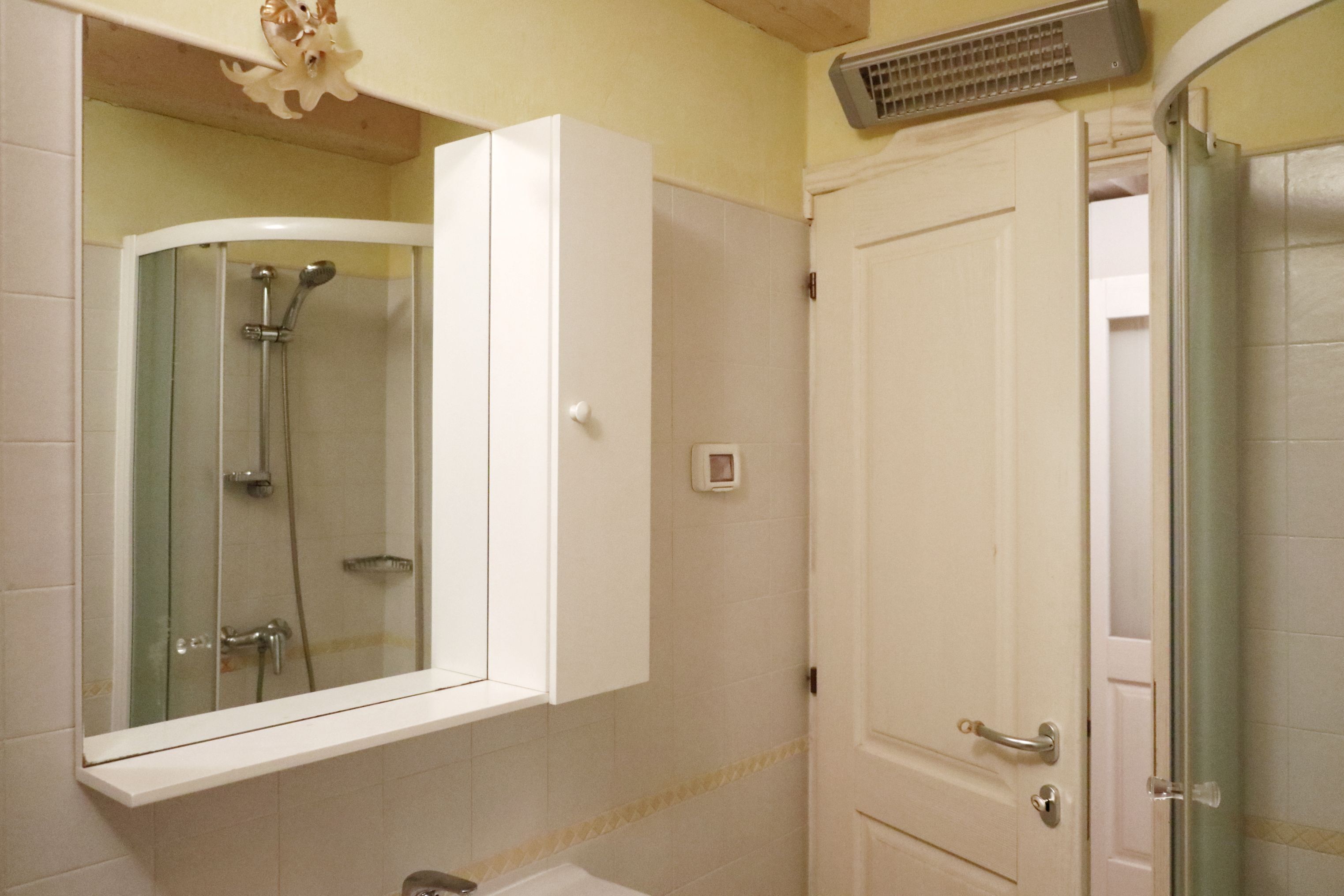 Une salle de bain avec une douche à parois de verre, un meuble blanc et une porte dotée d’une poignée.