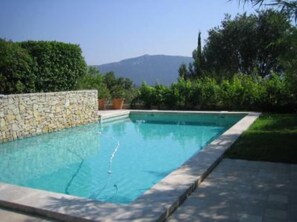A rectangular swimming pool with a stone wall on one side, surrounded by greenery and a clear sky. - House / Villa - Gemenos (Gémenos)