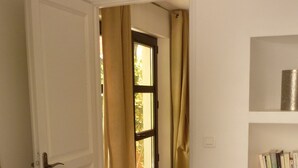 A bedroom with a bed, a dresser, a door leading to another room, and a shelf with books.