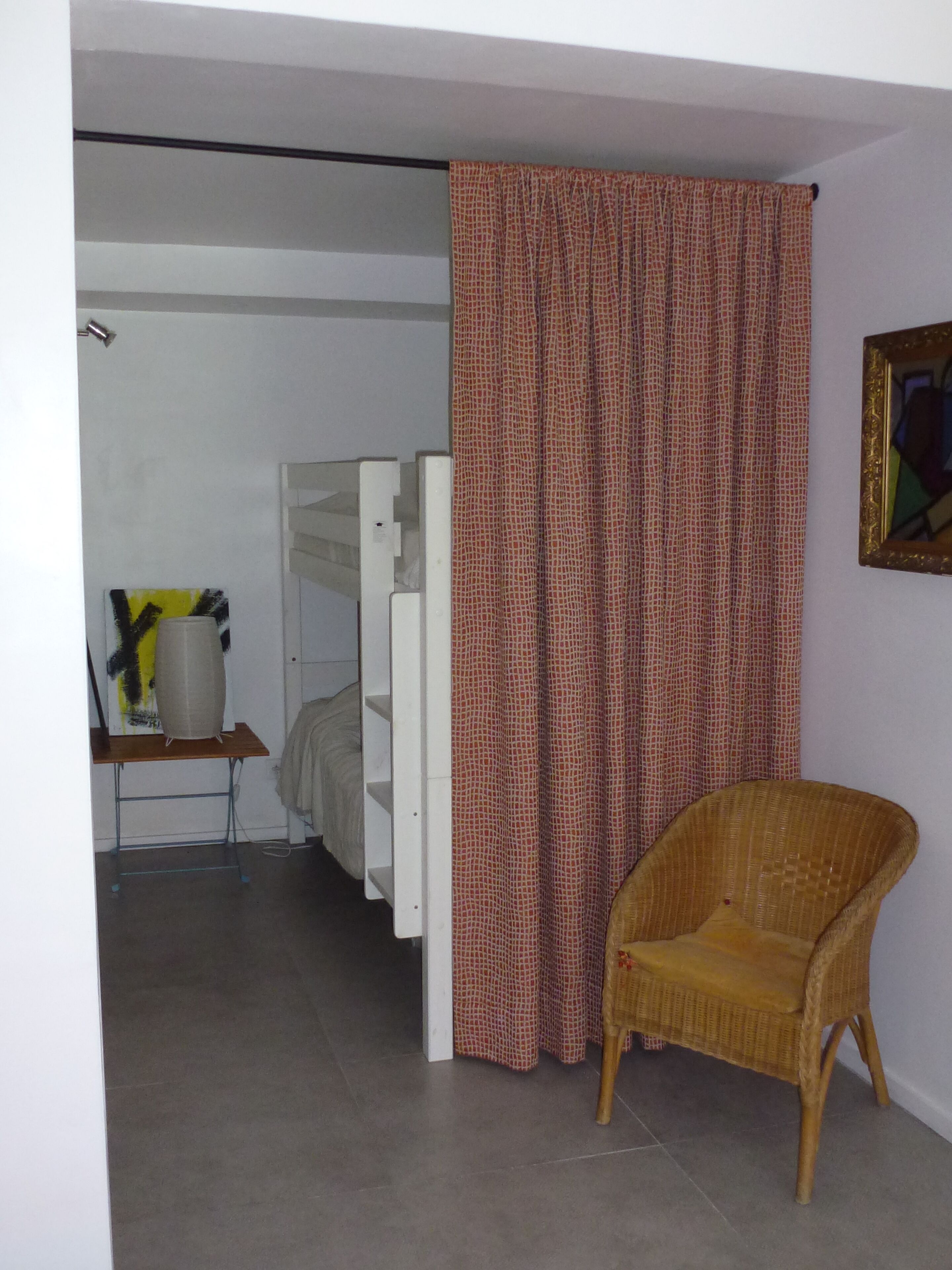 Een kamer met een bed, een stoel, een gordijn en een schilderij aan de wand.