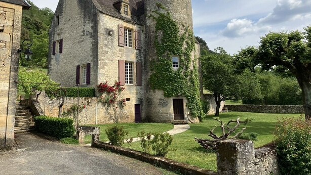 A stone building with a tower, a garden, and a pathway leading to the entrance.