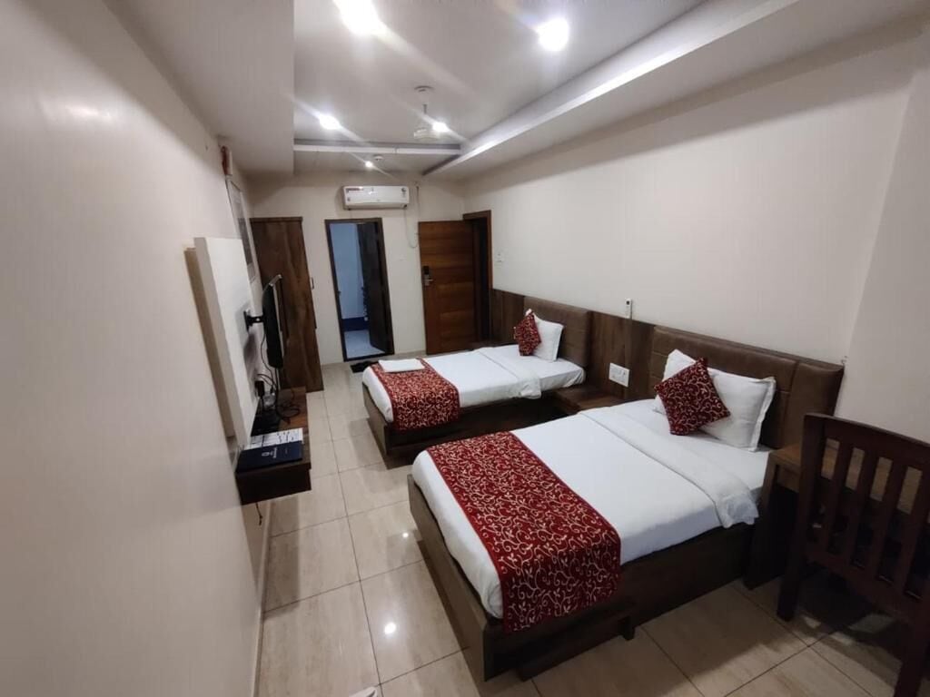 A hotel room with three beds, a wooden headboard, a small desk, and a wall-mounted air conditioning unit.