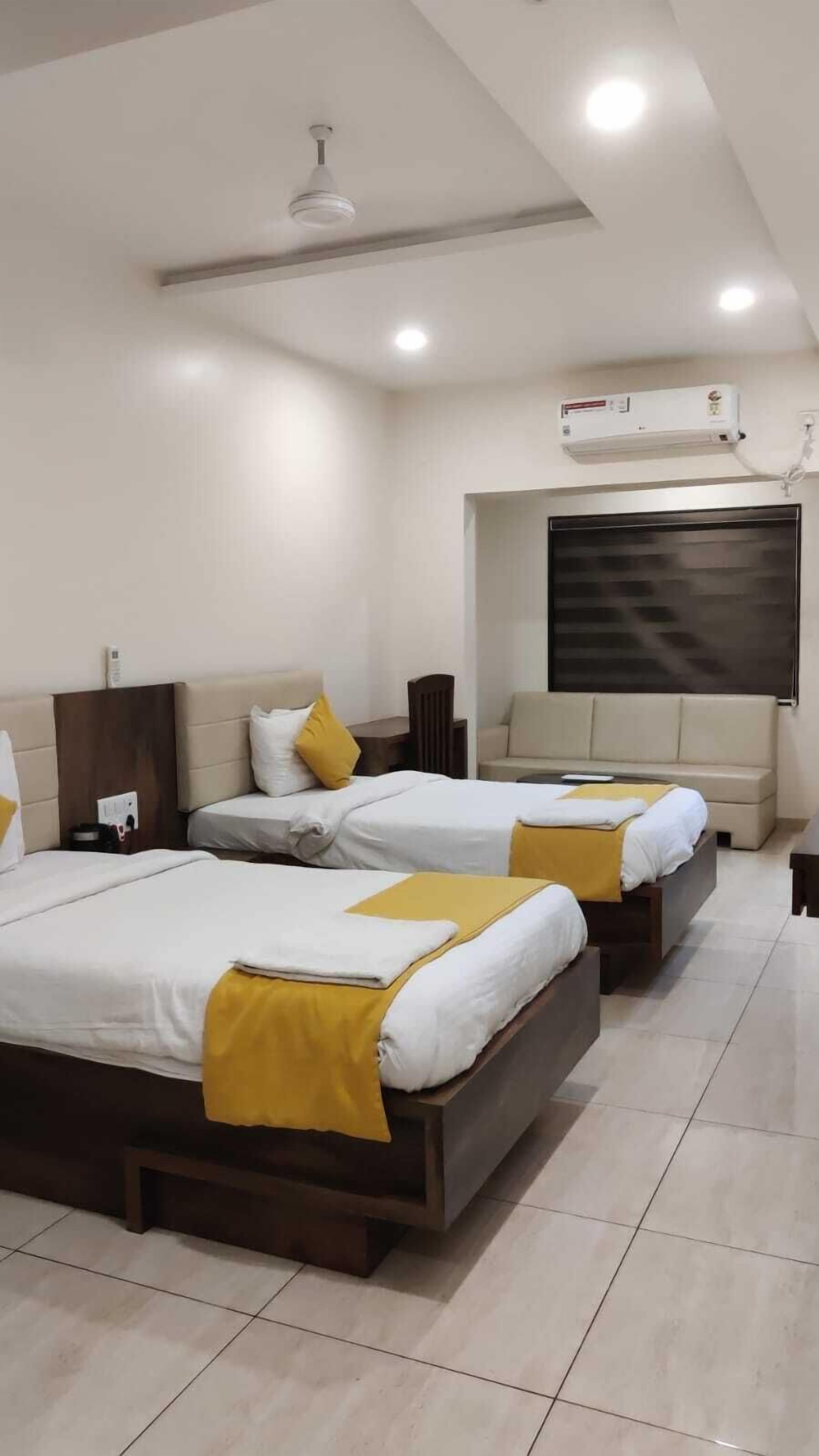 A hotel room with two beds, a ceiling fan, a large window, and a wall-mounted air conditioner.