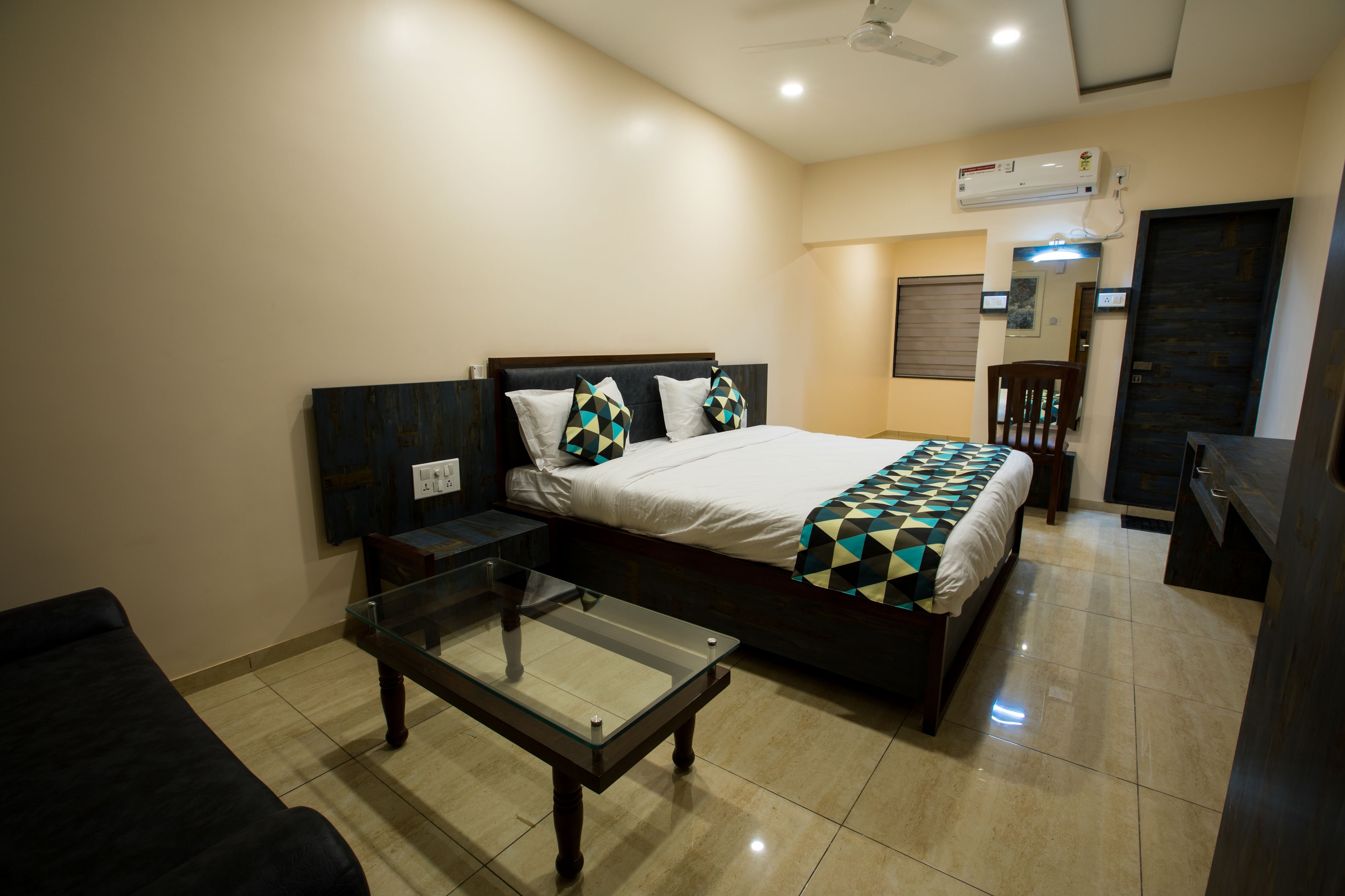 A hotel room with a bed, a glass-top table, a chair, and a desk.