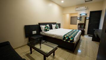 A hotel room with a bed, a glass-top table, a chair, and a desk.