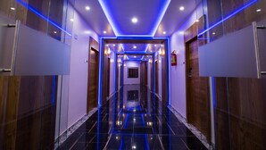 Un corridoio moderno di un hotel con pavimento nero lucido, rivestimenti in legno sulle pareti e illuminazione blu soffusa.